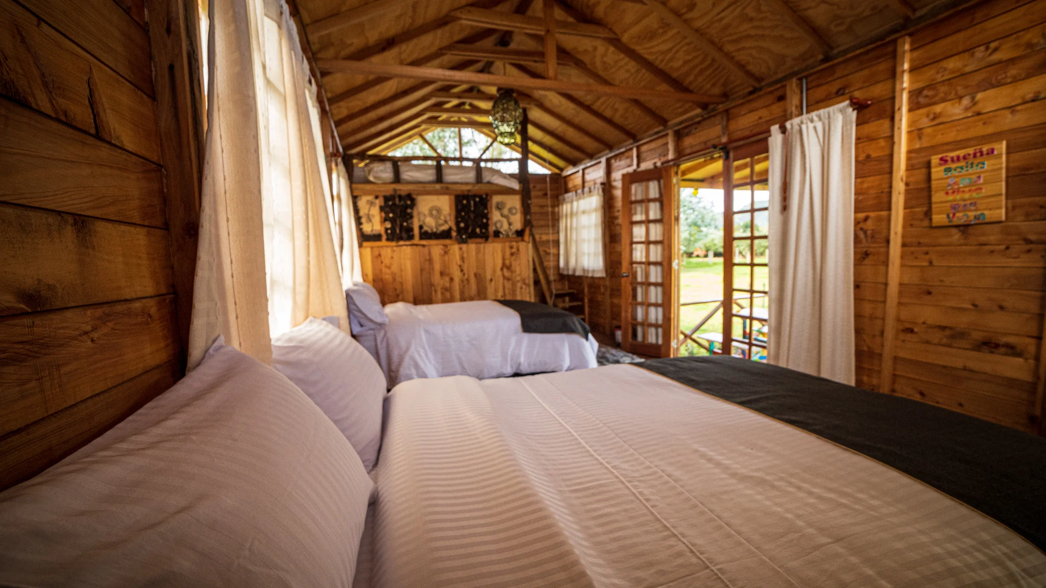 Interior acogedor de una cabaña glamping con camas dobles y vista al campo en El Nodo Glamping, Tenjo